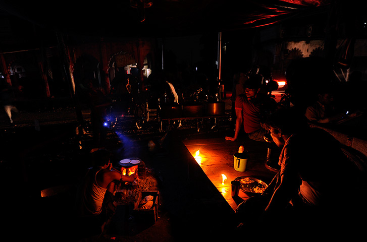 India blackout ends: A man prepares meal as others sit at a roadside shop on a dark street
