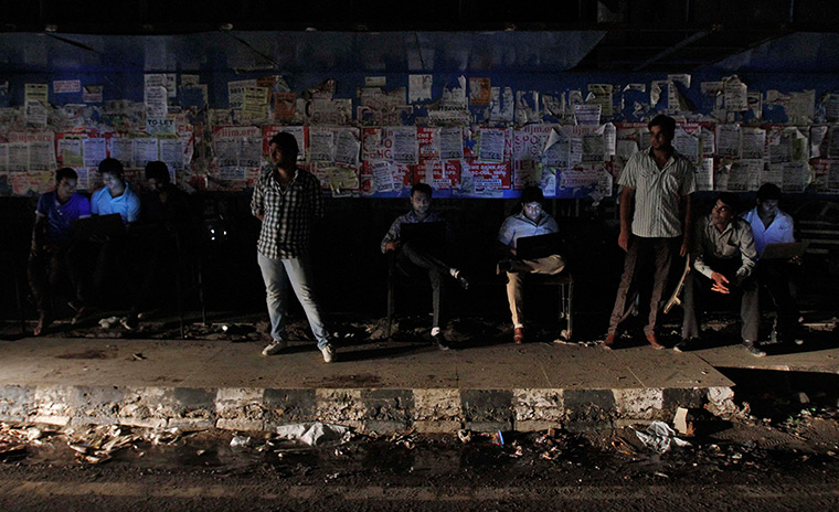 India blackout ends: Commuters work on their laptops as they wait for the bus
