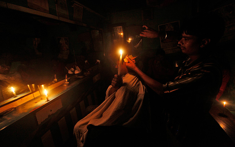 India blackout ends: A customer holds a candle as he gets his haircut at a barber's shop