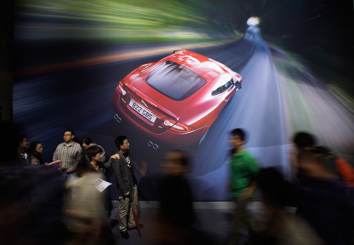 Week in Business: Visitors walk past a poster of a Jaguar XK at Auto China 2012 in Beijing