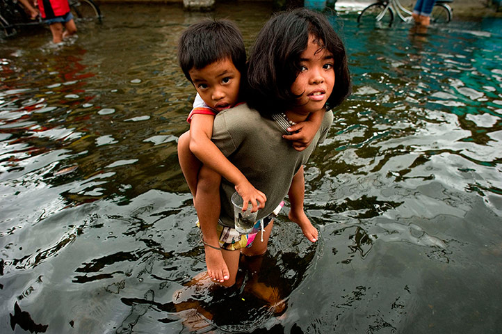 Manila flooding: A girl hold a boy on her back to help him through floods