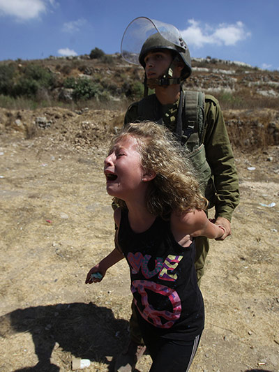 24 hours: An Israeli soldier holds a Palestinian girl back as she cries