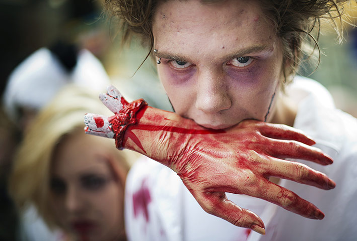 Zombie walk: A zombie holds a fake bloody hand in his mouth