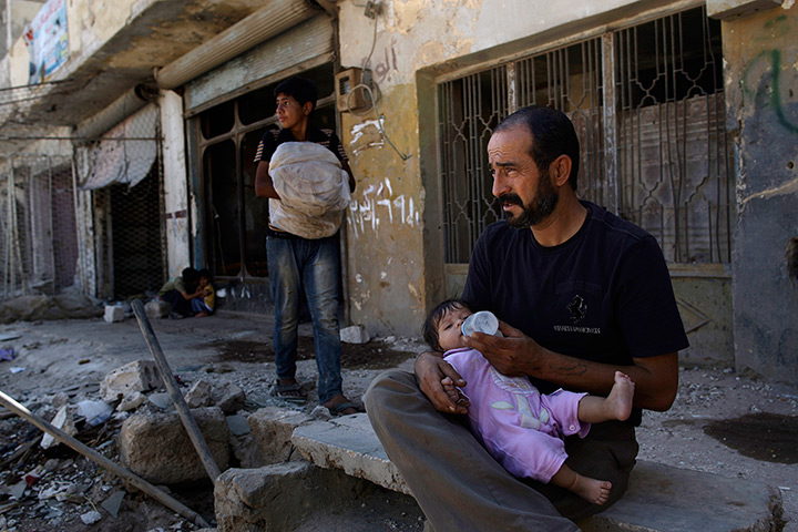 24 hours: Azaz, Syria: A man feeds his daughter outside his damaged house