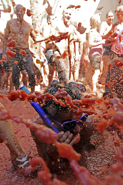 tomatina festival: A young man with a snorkel splashes himself on the ground