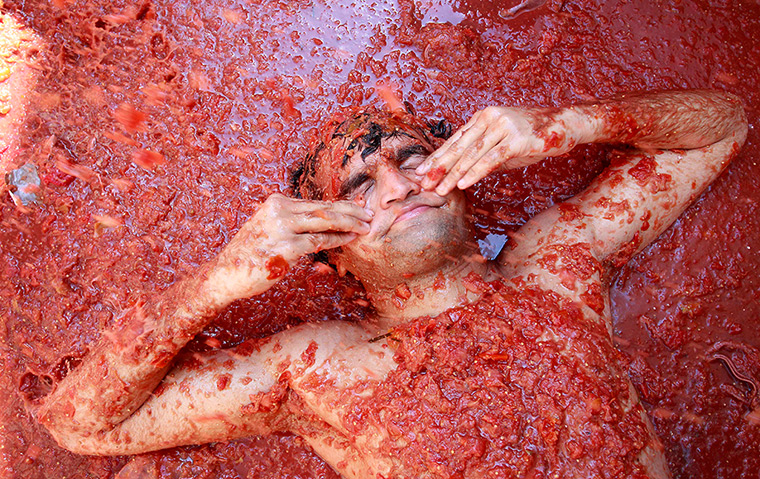 tomatina festival: A reveller wipes tomato pulp from his face