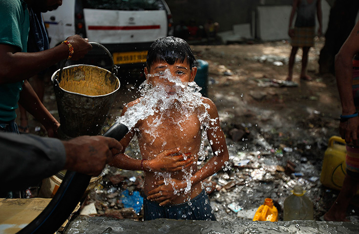 24 hours in pictures: A young Indian boy takes bath in water from a roadside pipe