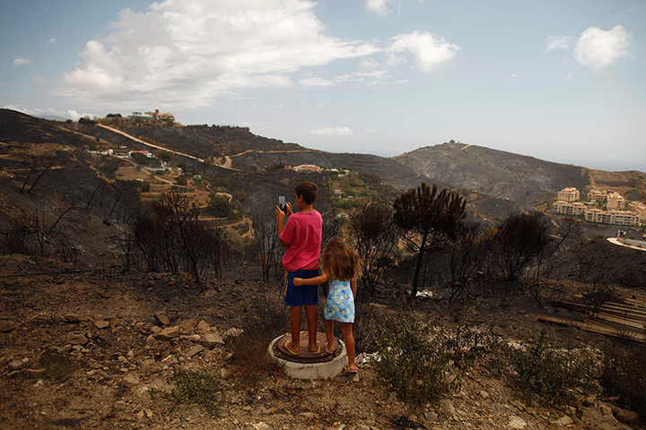 fires on costa del sol: A boy takes a picture of a burnt-out residential area in Calahonda 
