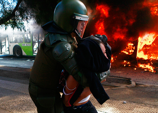 24 hours: Santiago, Chile: A girl is taken away by riot police as a bus burns