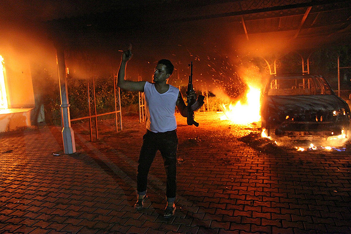 Benghazi protest: An armed man waves his rifle as buildings and cars are engulfed in flames