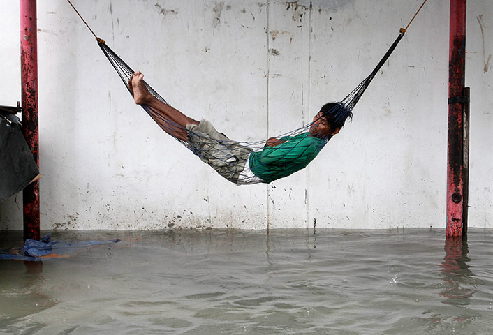 24 Hours: A worker sleeps on a hammock above a flooded street 