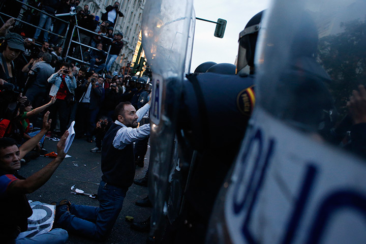 Madrid update: A demonstrator kneels before the riot police outside the Spanish parliament