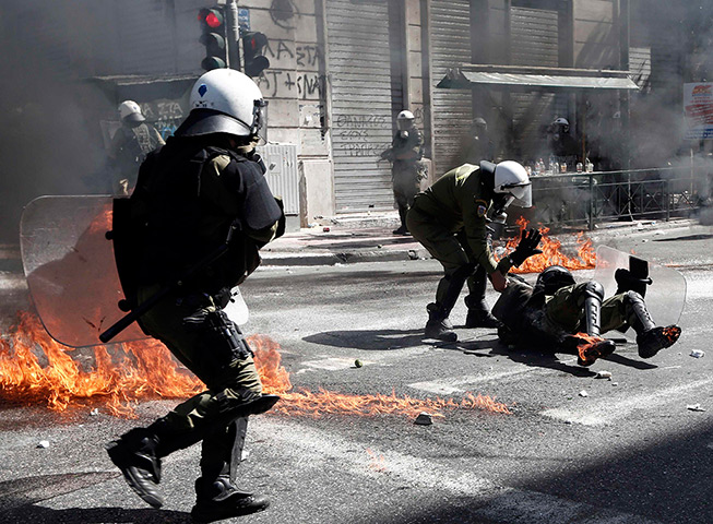 Greece protests update: A riot police officer is helped by a colleague after falling during clashes