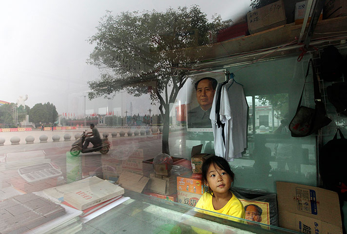 Twenty Photos: In Nanjie, China, a girl next to a portrait of the late Chairman Mao Zedong