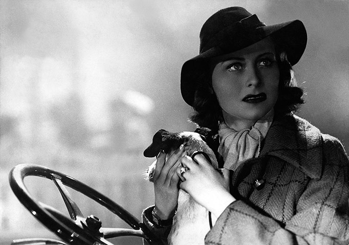 Black and white image of a woman at a steering wheel wearing a hat from French film Le Quai des Brumes