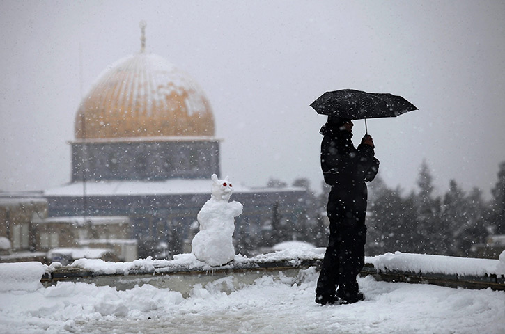 Snow in Jerusalem: A Palestinian man stands on a roof of a house near the Dome of the Rock