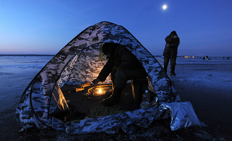 24 hours in pictures: A man sits in a tent while ice fishing at sunrise in the Lake Vileika