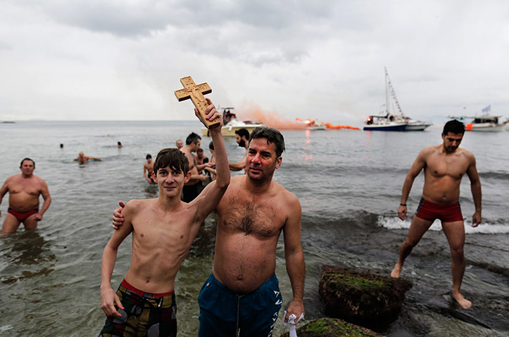 Epiphany Day: A youth holds up a cross after retrieving it from the water