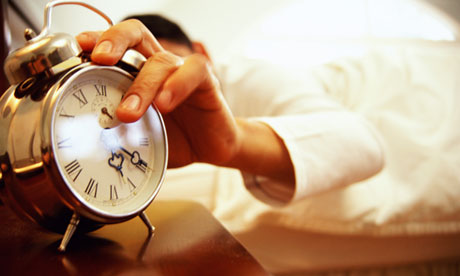 Man in bed reaching for alarm clock