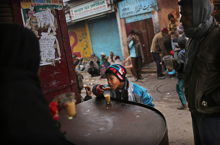 Cold weather in India: A young Indian boy eats a biscuit with his tea