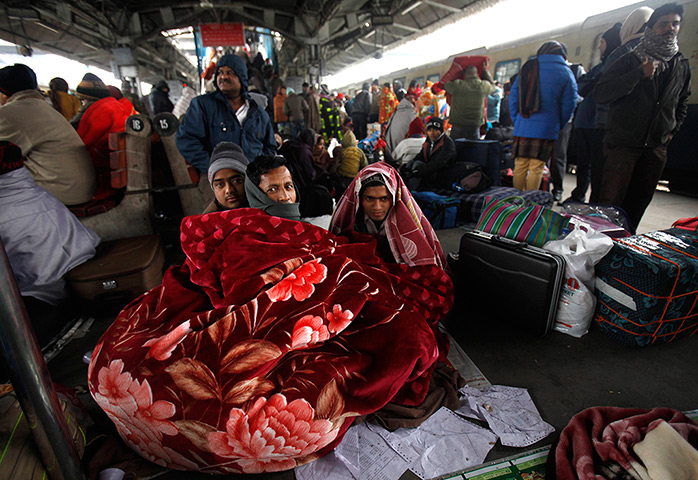 Cold weather in India: Passengers wrap themselves in a blanket as they wait to board a train