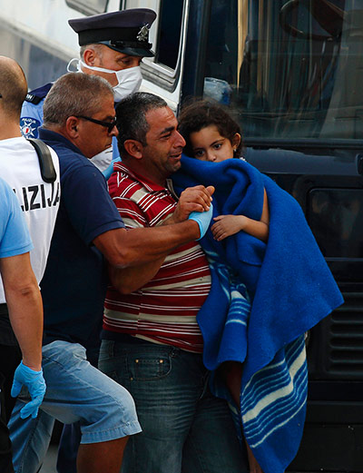 Malta: A rescued migrant cries as he carries his child to a police bus after disembarking from a Maltese ship 