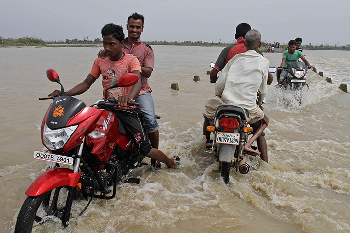 Cyclone Phailin: Men ride through floods in Berhampur, in the eastern Indian state of Orissa