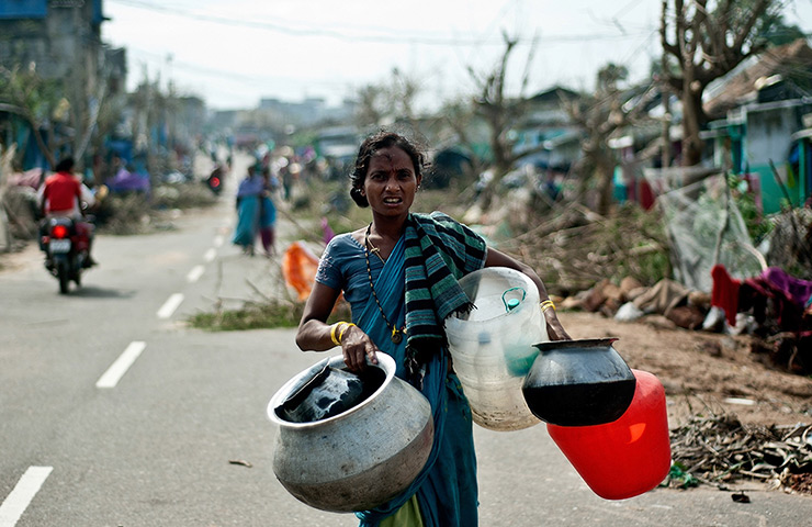 Cyclone Phailin damage: A woman carries empty water pots at the fisherman's colony in Gopalpur 