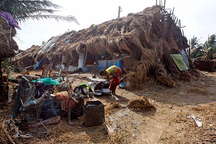 Cyclone Phailin damage: A villager washes utensils near her damaged house in the cyclone hit villag