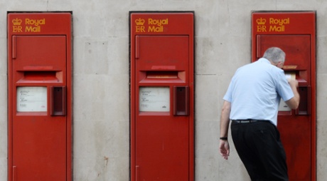A man posts a letter at Royal Mail post boxes outside a Post Office in central London.