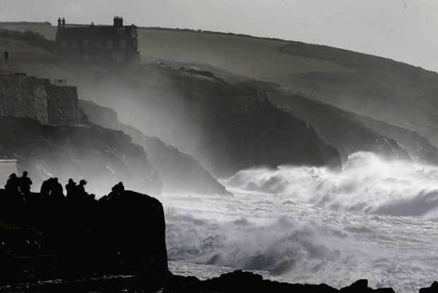 Members of the public witness a dramatic sea, produced by storm force winds break along the coast at Porthleven in Cornwall, England.