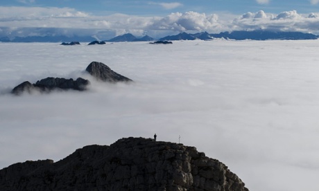 A man watches a sea of clouds as he stands on a side summit of the Saentis mountain in Urnaesch near Appenzell, Switzerland.