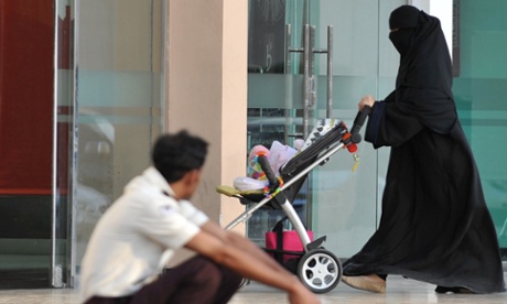 A Saudi woman walks past a foreign worker at a shopping mall.