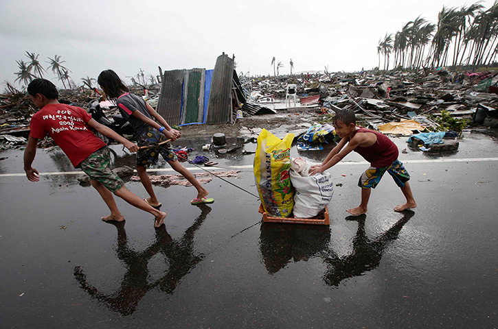 Typhoon hits Tacloban: residents carry relief goods past damaged homes 