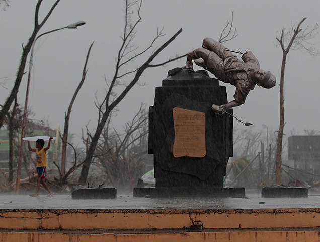 Typhoon Haiyan: A young survivor uses a plastic cover to protect him from rain as he passes