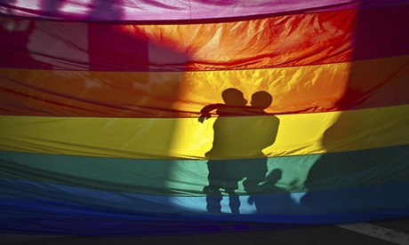 A couple hugs on the other side of a gay pride flag