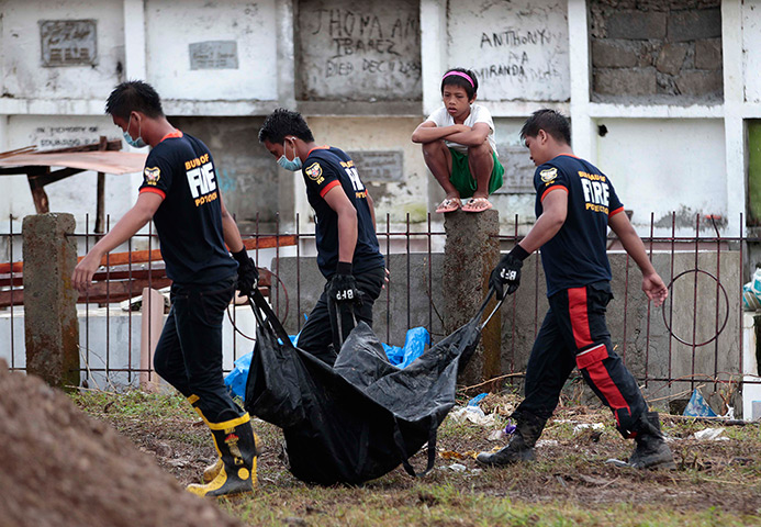 Philippines survivors: A young boy watches firemen carry victims of typhoon Haiyan at a mass buria