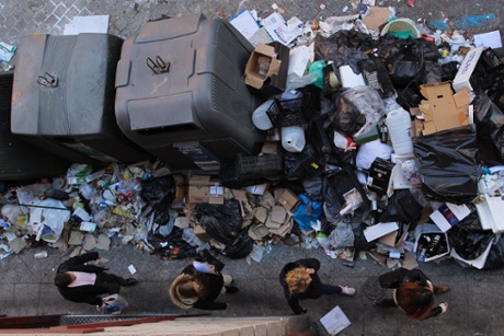 Women walk past a pile of rubbish surrounding trash containers during the eleventh day of a garbage collectors strike, Madrid, Spain, Friday, Nov. 15, 2013.