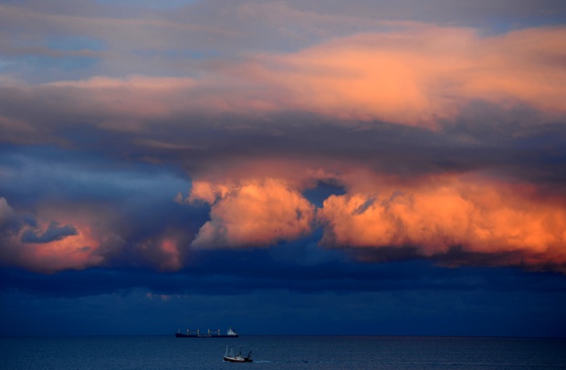A fishing boat heads out to sea as the sun sets against a stormy sky on north east coast of the UK near Tynemouth. 