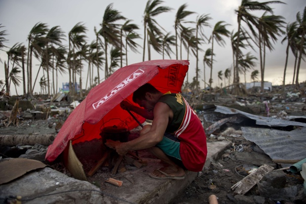 A man uses an umbrella to shelter from the wind as he tries to light a fire amid the rubble of destroyed homes in Tacloban.