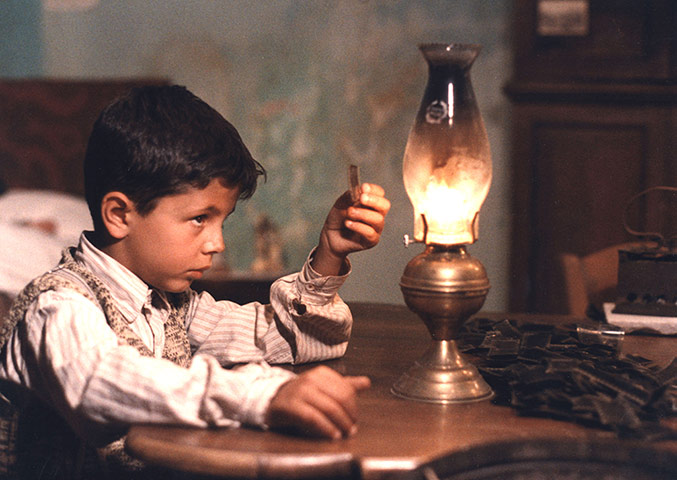 Cinema Paradiso gallery: Cinema Paradiso: Salvatore examines a piece of film next to a gaslamp