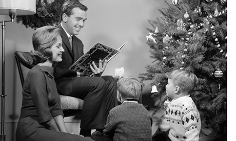 1960s Family Father Mother Two Sons Sitting By Christmas Tree In Living Room Reading A Book