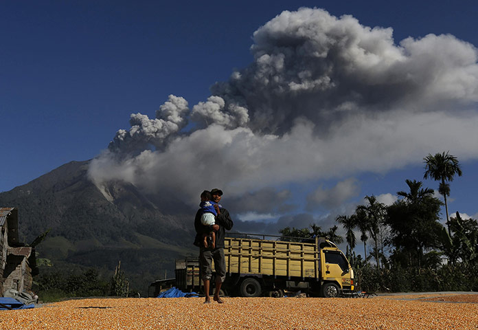 20 Photos: A man holds his son with Mount Sinabung spewing ash in the background