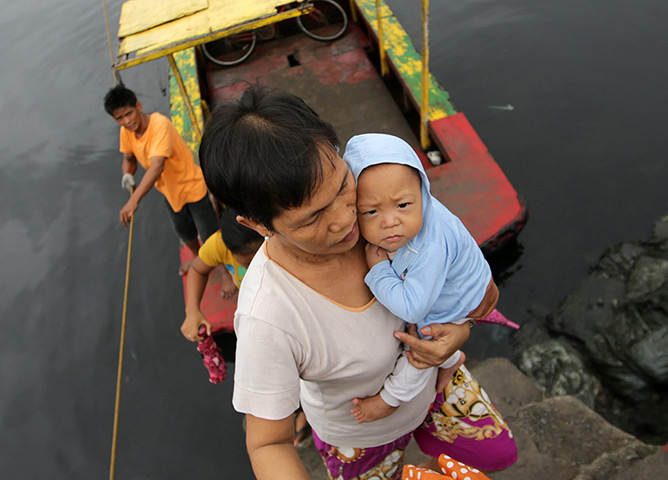 Typhoon: A Filipino resident carries a baby as they cross a river at a coastal villa