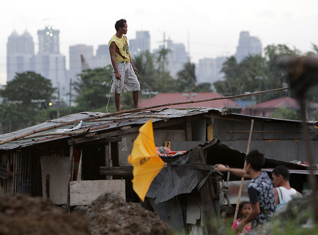Typhoon updated: A Filipino resident stands on a roof of a home with a backdrop of a cloudy 
