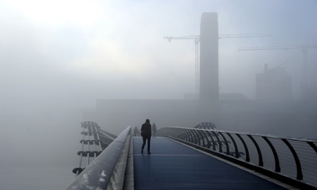 People walk through thick fog at the Millennium Bridge over the River Thames in London.