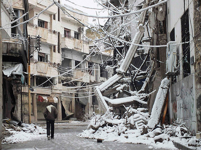 Winter in Syria: A man walks past debris from damaged buildings covered with snow in a besie