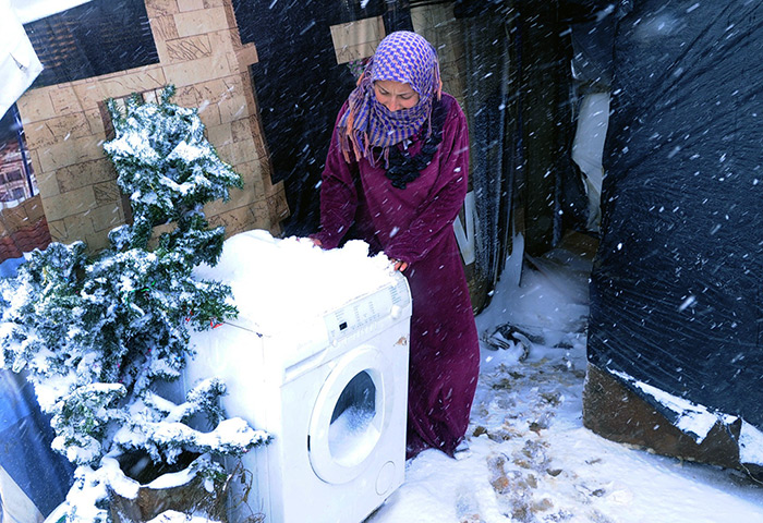 Winter in Syria: A Syrian refugee tries to move a washing machine outside her tent to protec