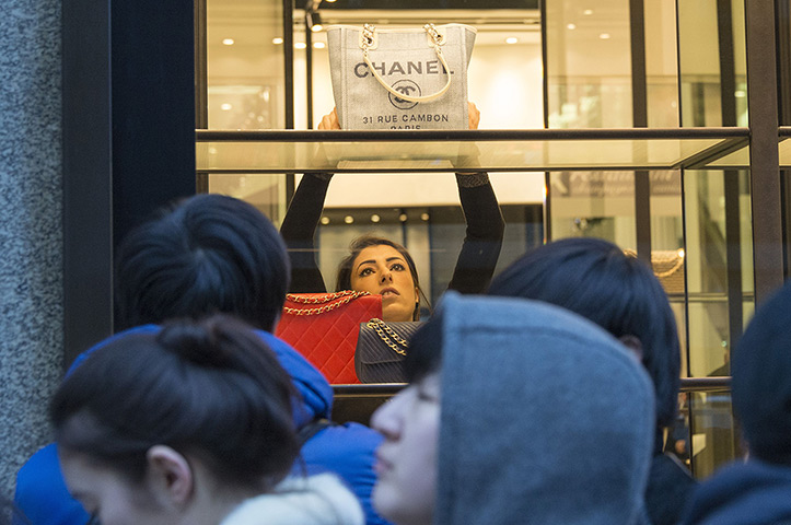 Boxing day sales: Shop assistant puts a Chanel bag on the window display as customers queue o