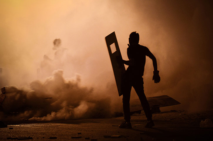 20 Photos: A Bahraini protestor stands amidst teargas fired by riot police in Diraz